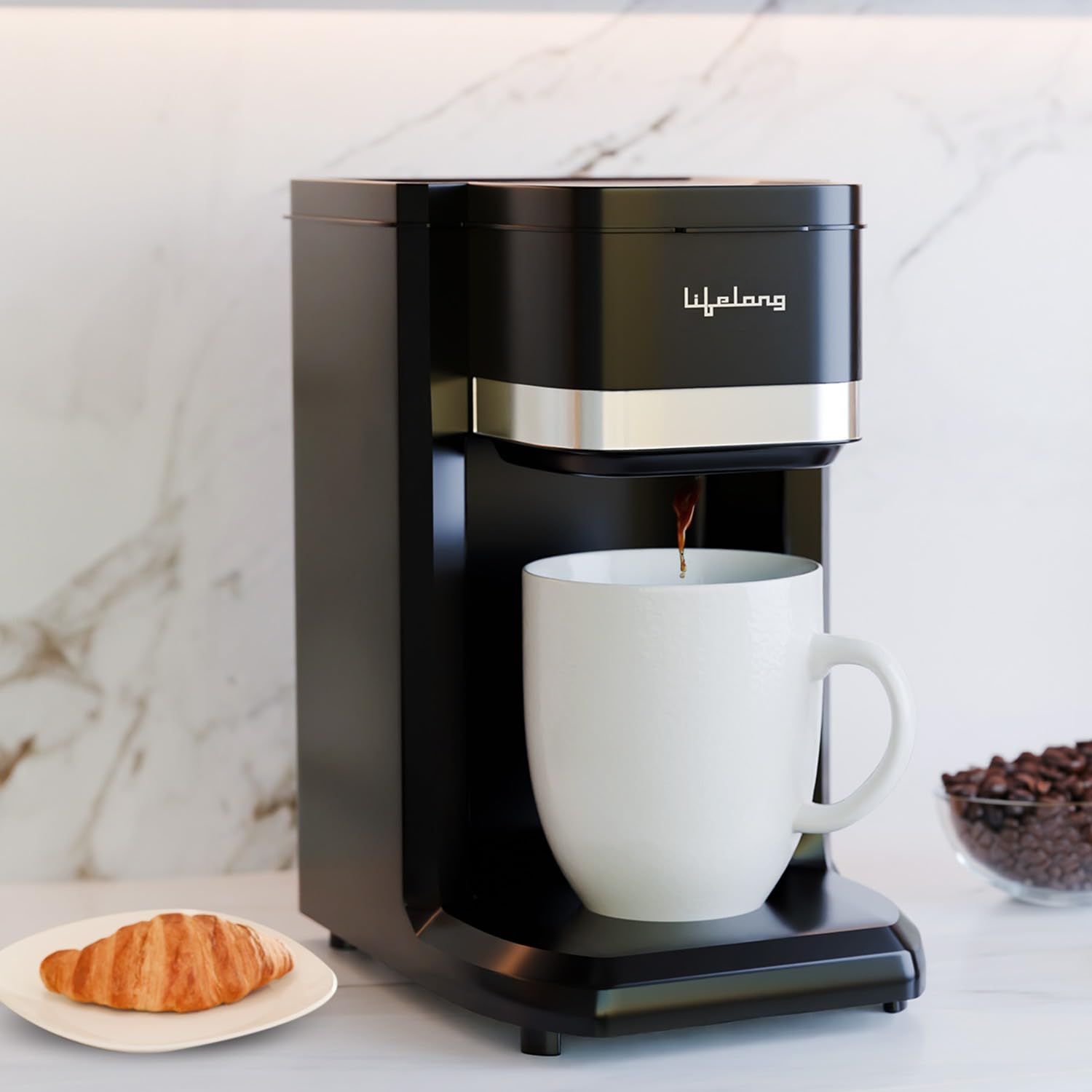 A black coffee maker with a silver band and Arabic script logo, dispensing coffee into a white ceramic mug on a marble countertop, with a croissant and coffee beans nearby.