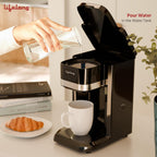 A black single-serve coffee maker with a white mug underneath, shown in a kitchen-like setting with a hand pouring water from a glass into the tank. A croissant and books sit on a plate beside it, and the brand name 'Lijelong' is visible on the machine.
