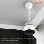 A modern white Orient Electric ceiling fan with three blades, shown installed on a white ceiling in a room. The fan has a sleek cylindrical motor housing with a black circular faceplate featuring a blue light indicator.