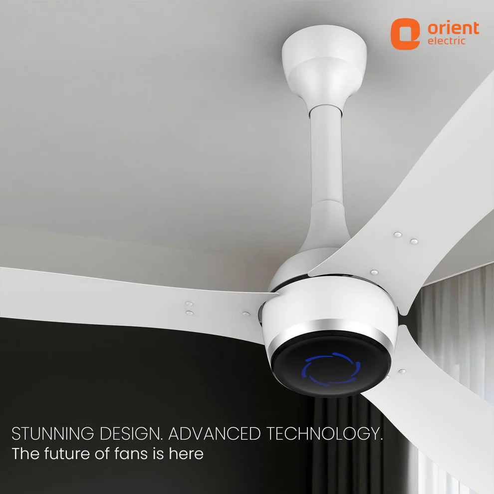 A modern white Orient Electric ceiling fan with three blades, shown installed on a white ceiling in a room. The fan has a sleek cylindrical motor housing with a black circular faceplate featuring a blue light indicator.