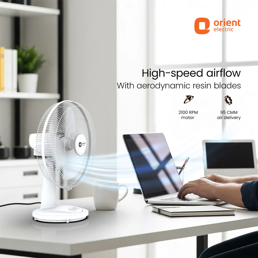 Orient Electric fan on a desk with a laptop and person using it, in an office setting.