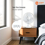 Table fan on a wooden nightstand with 'Orient Electric' branding in a bedroom setting.