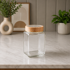 Premium square glass pantry storage jar with a wooden airtight lid placed on a modern marble countertop in a minimalist kitchen setting. Transparent glass container ideal for storing spices, grains, snacks, dry fruits, tea, coffee, and pantry essentials.